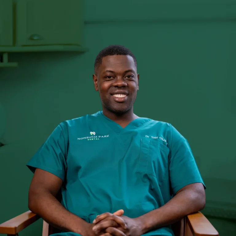 Dr Tobi seated in a dental clinic with dental chair in the background.